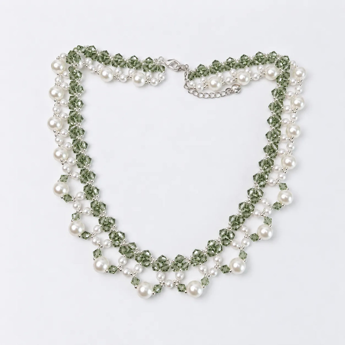 A multi-strand beaded necklace featuring green faceted beads, white faux pearls, and silver-toned metal links, displayed on a clean white background.