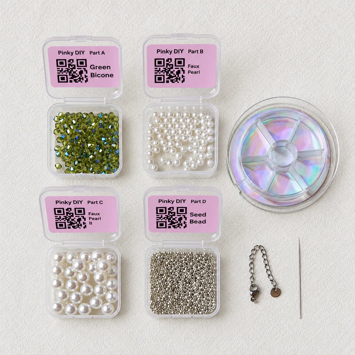 DIY bead craft kit components arranged on a light textured background, including six labeled plastic containers with green iridescent beads, white faux pearls, silver seed beads, a spool of iridescent discs, a chain, and a needle.