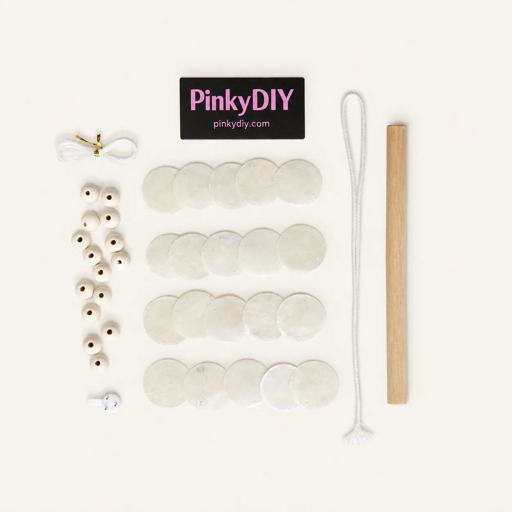 DIY beaded necklace kit from PinkyDIY, featuring white disc beads, white seed beads, a wooden mallet, a white cord, and a black brand label on a clean off-white background.