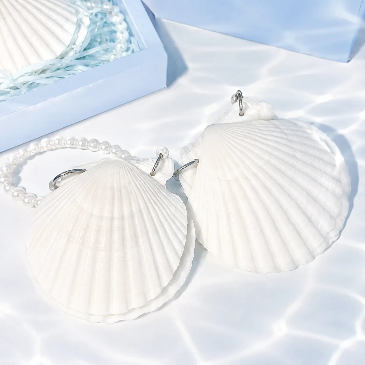 Shell-shaped earrings on a white surface with a light blue background